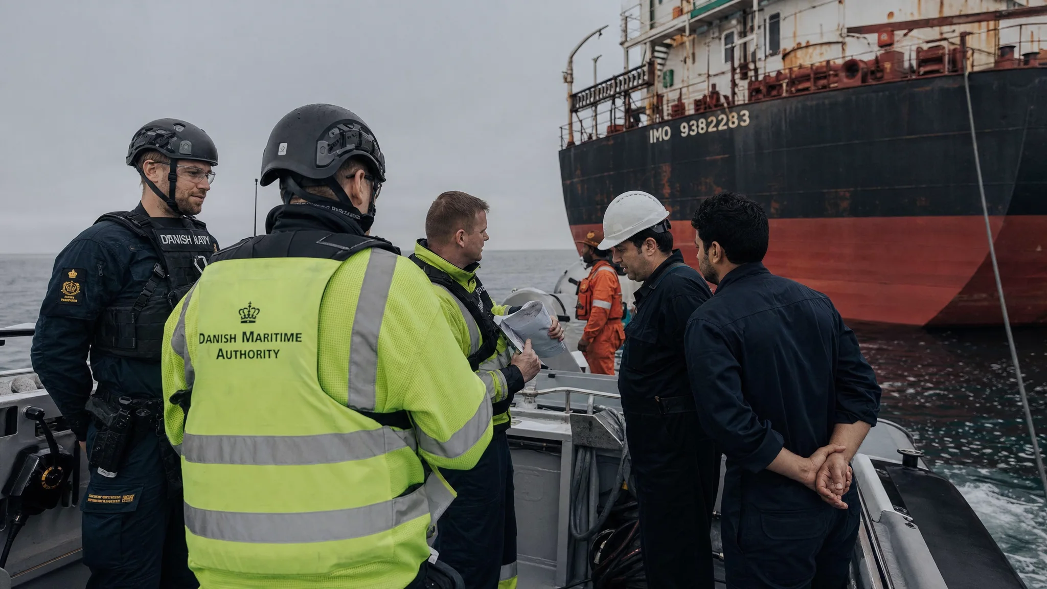 Danish authorities board a stationary oil tanker in the Great Belt, reviewing documents as a patrol vessel stands by in overcast Baltic weather. Danish authorities board a stationary oil tanker in the Great Belt, reviewing documents as a patrol vessel stands by in overcast Baltic weather.