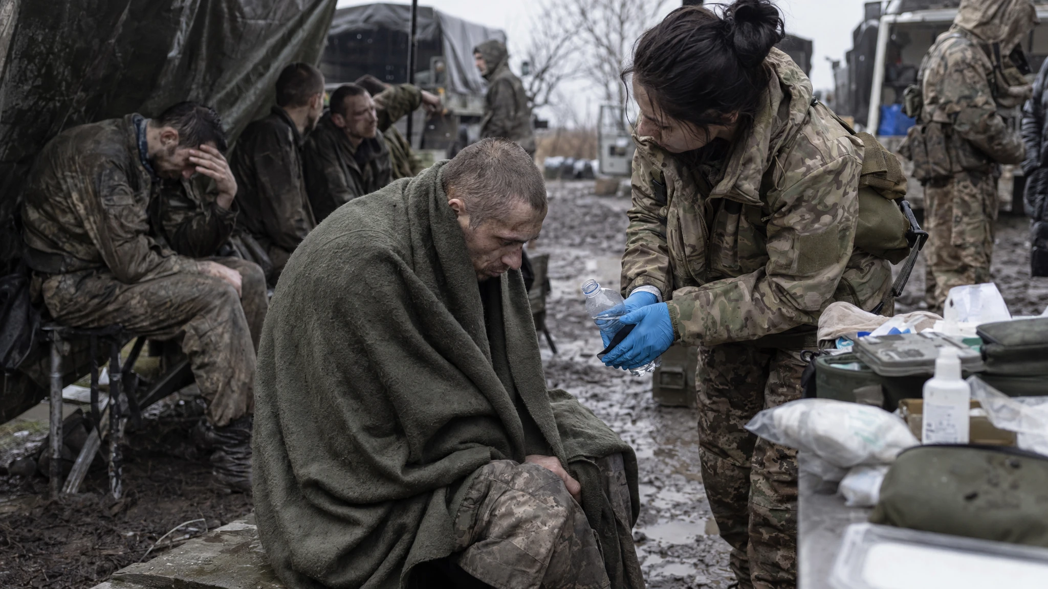 A Ukrainian medic checks an exhausted Russian prisoner of war as other captives wait at a muddy field medical station. A Ukrainian medic checks an exhausted Russian prisoner of war as other captives wait at a muddy field medical station.